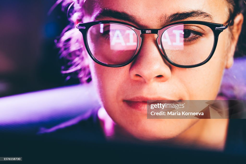 Woman using artificial intelligence technology on laptop with glasses reflection.