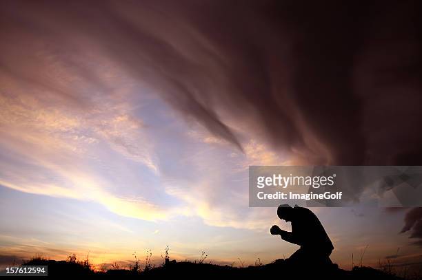 silhouette of unrecognizable caucasian man praying during storm - bidden stockfoto's en -beelden