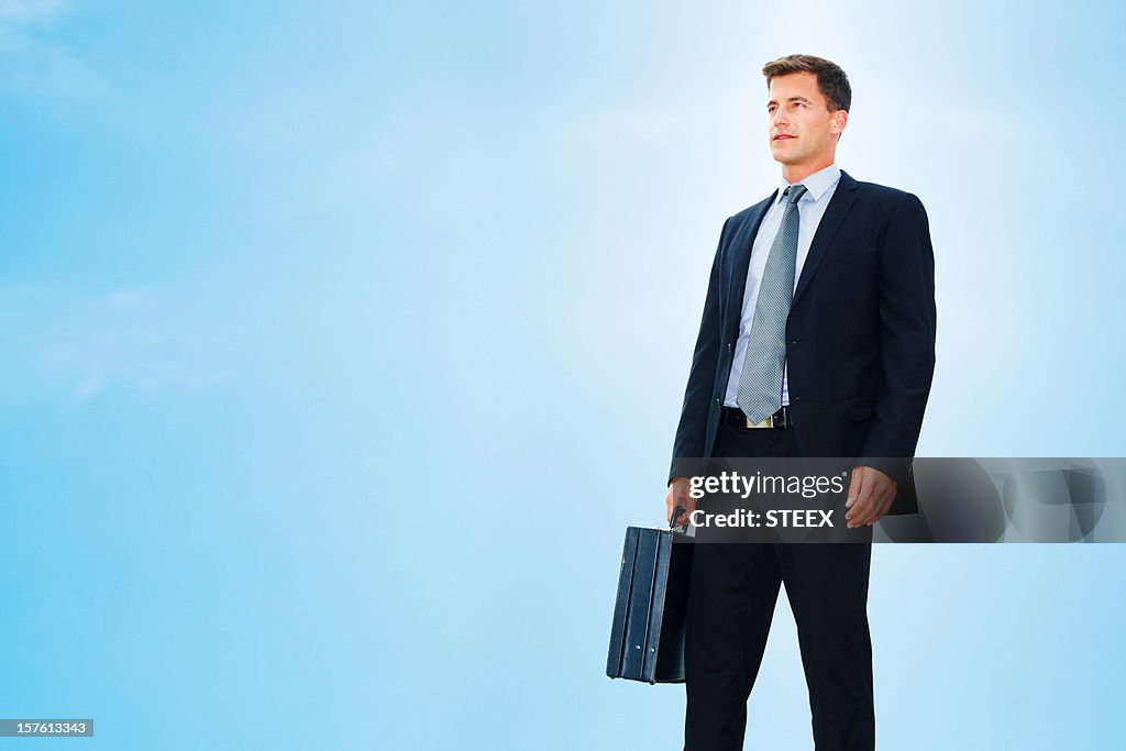 Confident mid adult businessman standing isolated against blue sky
