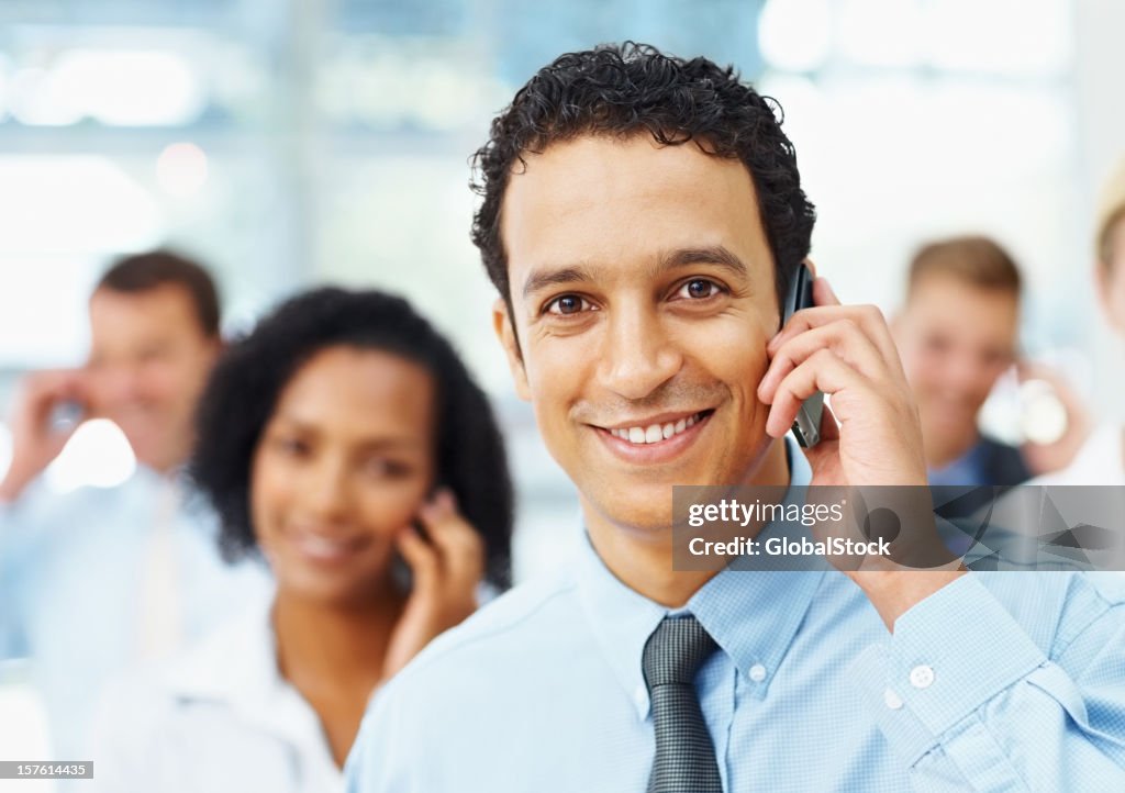 Happy business man speaking on phone with colleagues at back