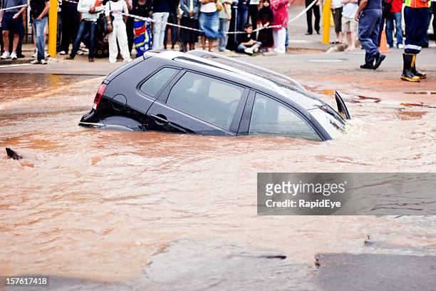 auto zieht unter schlammigen wasser in der lichtdurchfluteten street - sinkhole stock-fotos und bilder