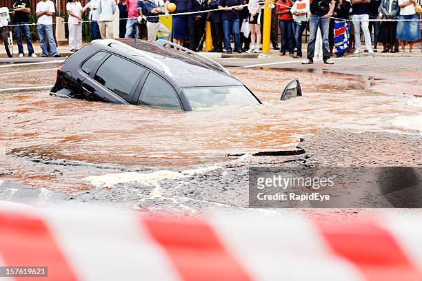 behind police cordon tape, a car slides into  muddy sinkhole - sinkholes stockfoto's en -beelden