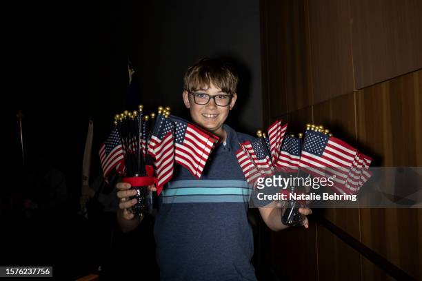 Parker McDowell 13, helps hand out small American flags to attendees at a naturalization ceremony at Grand Teton National Park August 4, 2023 in...