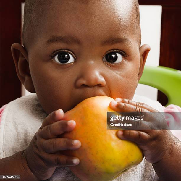 african descent baby girl eating apple, bib, high chair - eating with a bib stock pictures, royalty-free photos & images