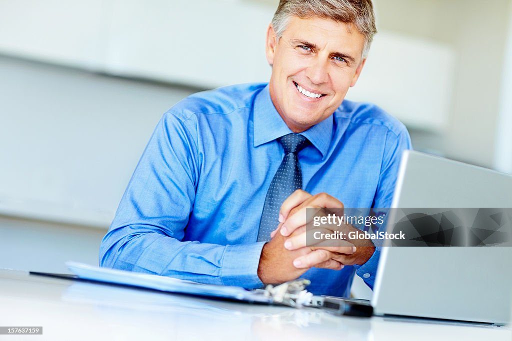 Happy executive with hands clasped sitting in front of laptop