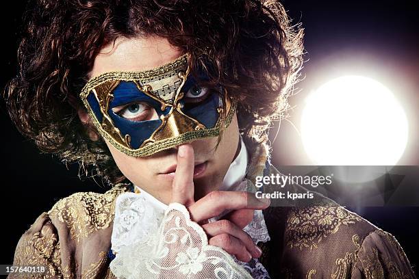 a man in a venetian mask putting a finger to his mouth - venetiaans masker stockfoto's en -beelden