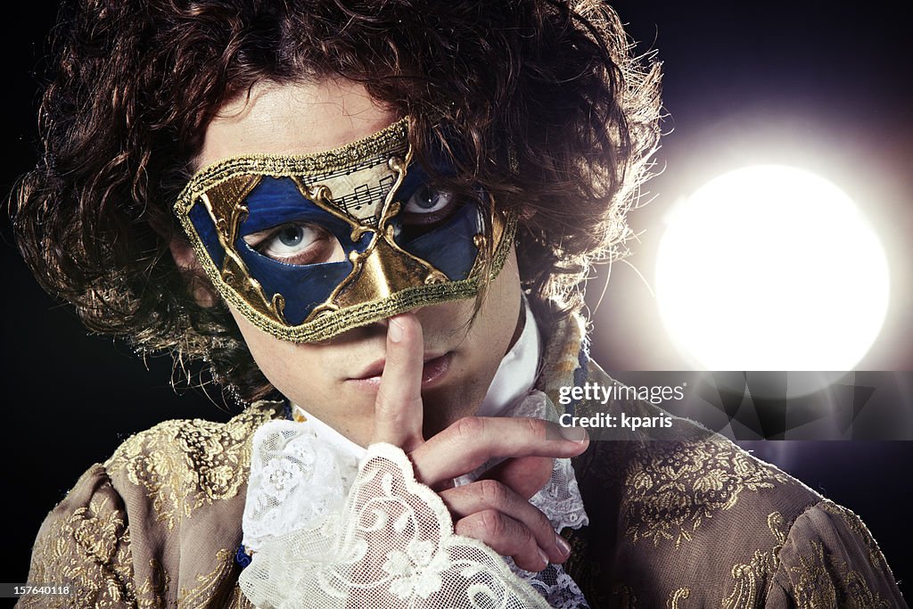 A man in a Venetian mask putting a finger to his mouth