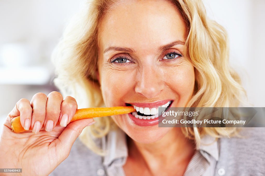 Happy mature woman eating a carrot