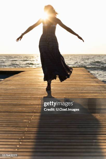 a woman in a dress on a dock with her arms spread - woman leg spread stock pictures, royalty-free photos & images