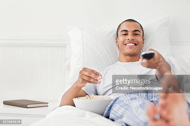 jeune homme regardant la télévision au lit - young man to bed photos et images de collection