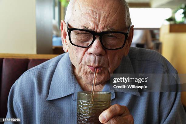 老人男性の目を細めるを飲み水からストロー - water glasses ストックフォトと画像
