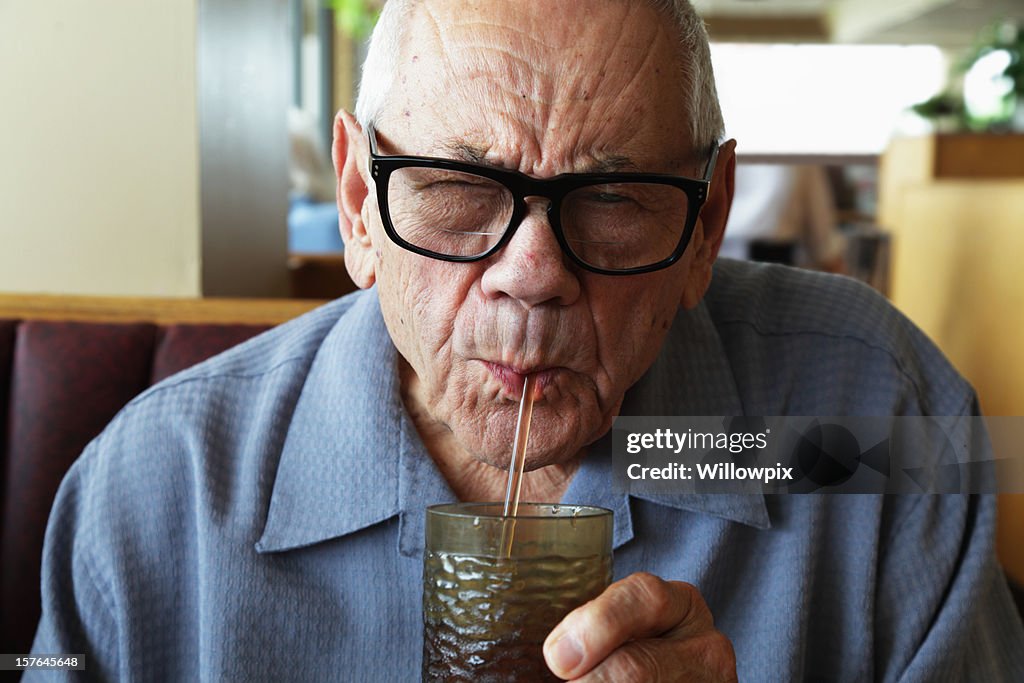 Senior Man Squinting While Drinking Water Through Straw