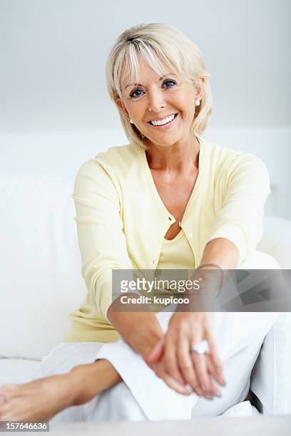relaxed mature woman sitting in couch against grey - mature female models stock pictures, royalty-free photos & images