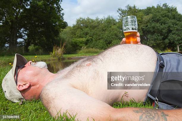 obese hombre con un vaso de cerveza para tomar el sol - pot belly fotografías e imágenes de stock