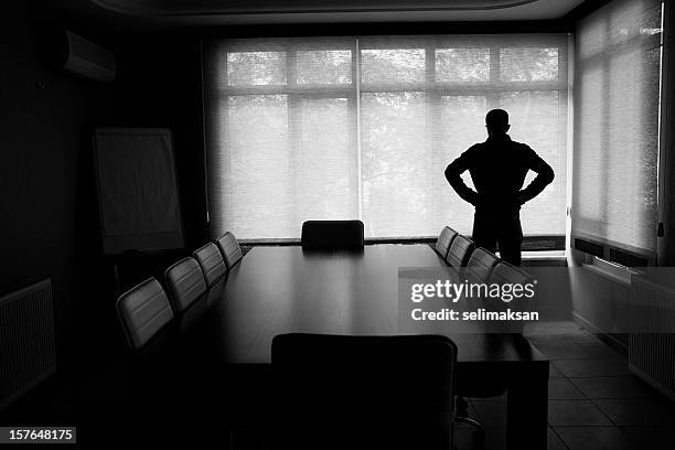 silhouette of lonely businessman standing by boardroom table in office - faillissement stockfoto's en -beelden