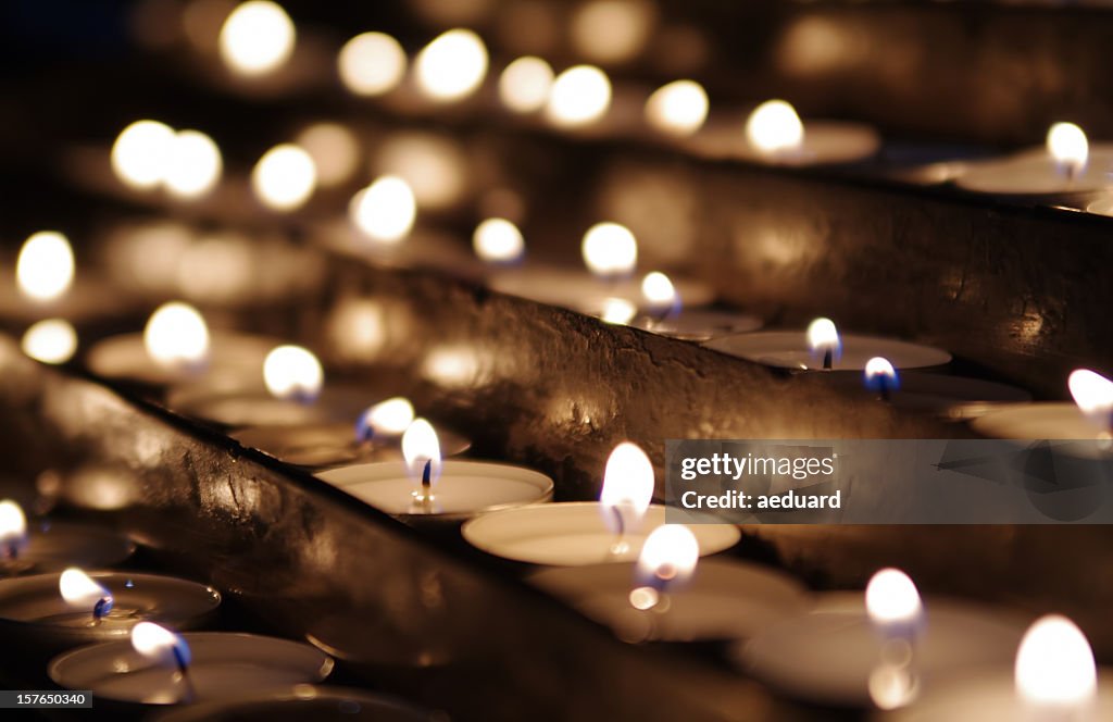 Rows of lit tea candles in sepia tones