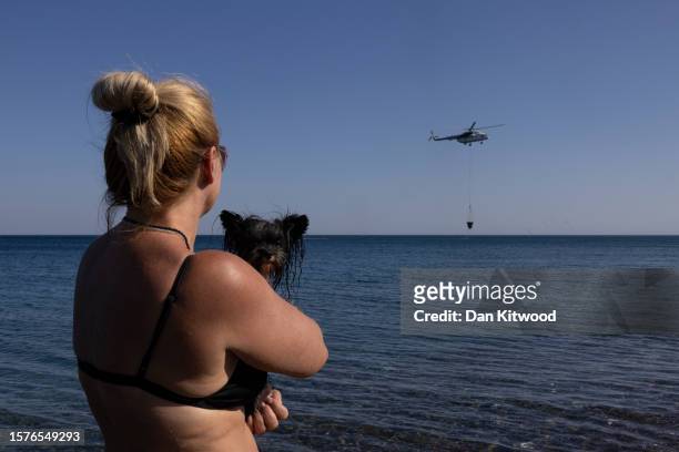 Holiday maker from the Czech Republic and her dog Olivier watch as a helicopter scoops up water to drop on wildfires on July 28, 2023 in Gennadi,...