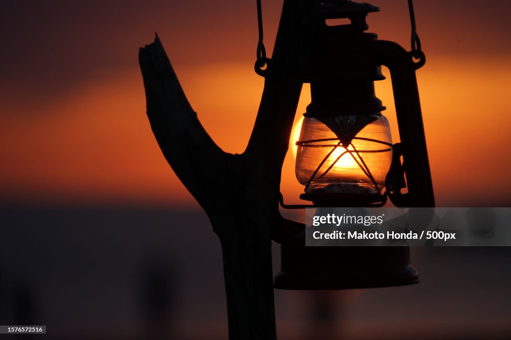 Close-up of silhouette of hand holding lantern against sky during sunset