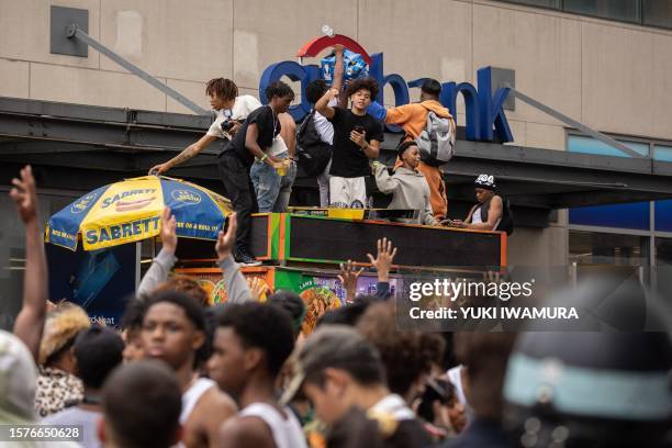 People stand on top of a street vendor's cart during riots sparked by Twitch streamer Kai Cenat, who announced a "givaway" event, in New York's Union...