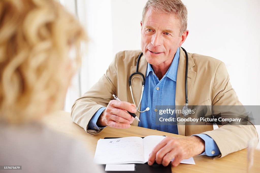 Mature doctor talking with his female patient sitting at desk