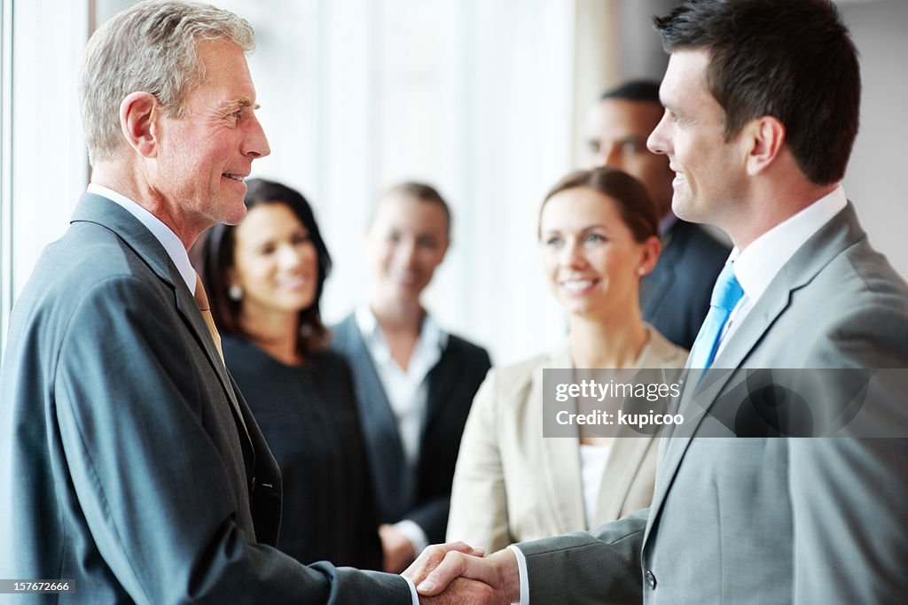 Two business men shaking hands with their teams in background