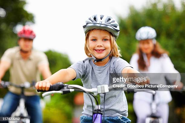 sportliche kleiner junge mit seinen eltern im hintergrund reiten fahrräder - two kids with cycle stock-fotos und bilder