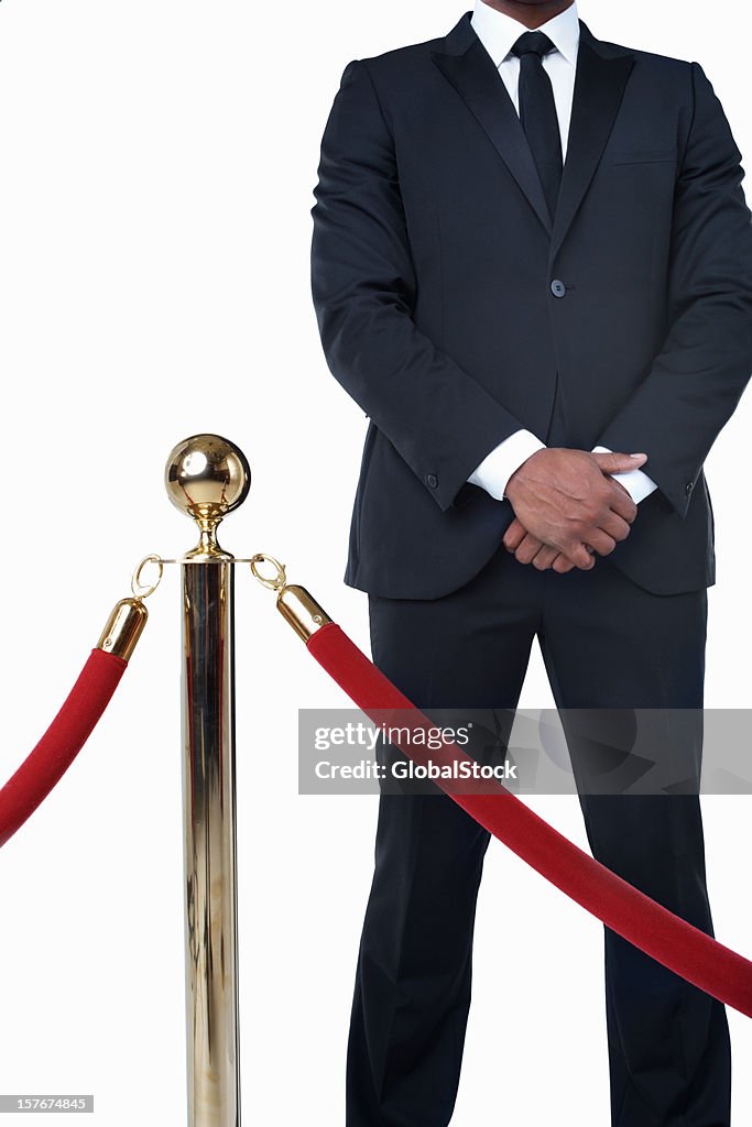 Bouncer in suit standing behind crowd control post against white