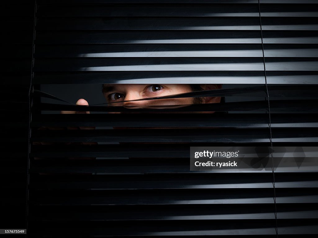 Mysterious Male Peering Out From Opening Behind Blinds