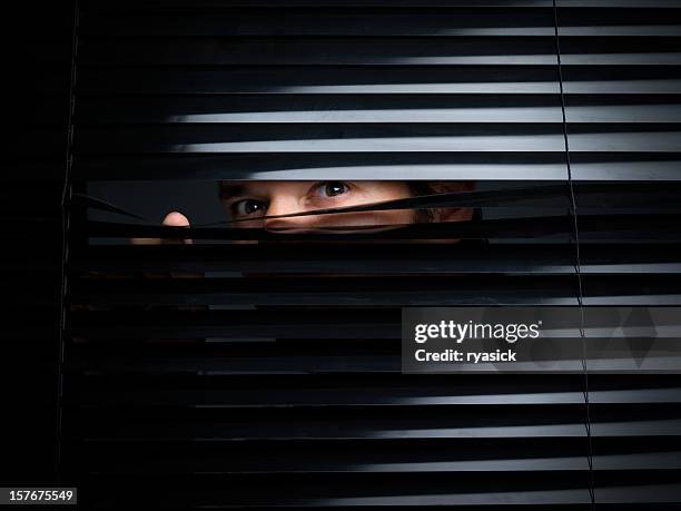 mysterious male peering out from opening behind blinds - blinds stock pictures, royalty-free photos & images