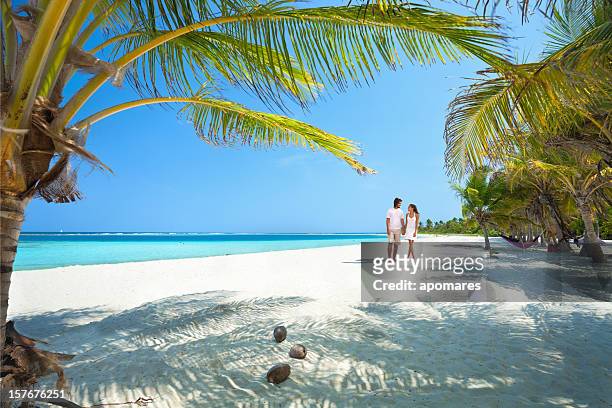young couple walking along a lonely tropical island beach - tropical beach couple stock pictures, royalty-free photos & images