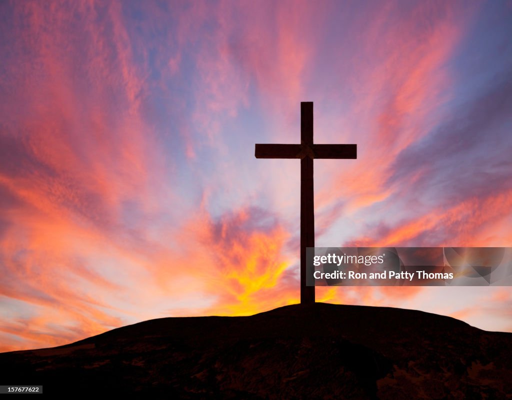 Silhouette of a wooden cross on a hill with a sunset