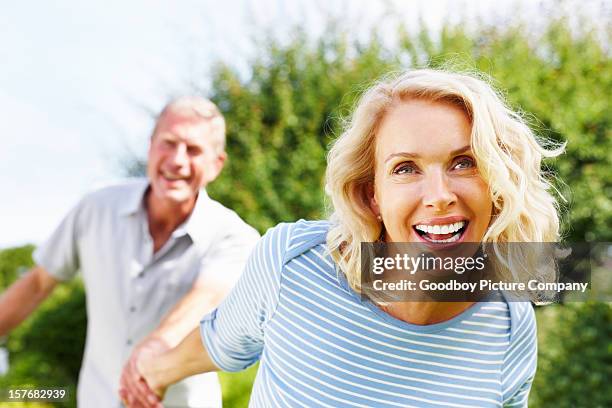 cheerful woman holding hand of a senior man against sky - senior couple smiling stock pictures, royalty-free photos & images