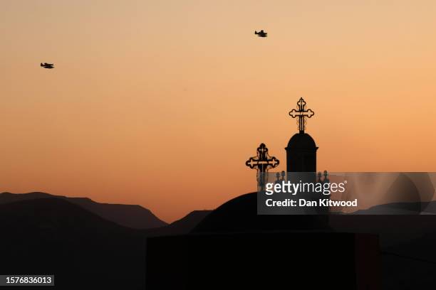 Greek Orthodox Church is silhouetted as firefighting planes return to base at sunset on July 28, 2023 in Asklipio, Rhodes, Greece. While firefighting...
