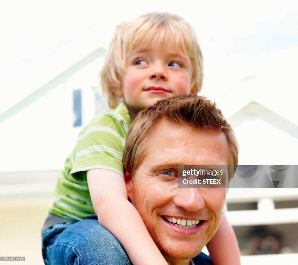 Happy mature man carrying his son in front of house