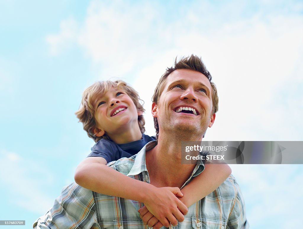Joyful mature man gives his son a piggyback ride