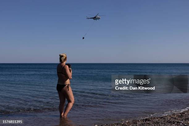 Holiday maker from the Czech Republic and her dog Olivier watch as a helicopter scoops up water to drop on wildfires on July 28, 2023 in Gennadi,...