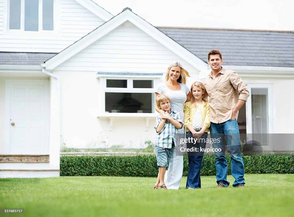 Four people standing on lawn in front of their house