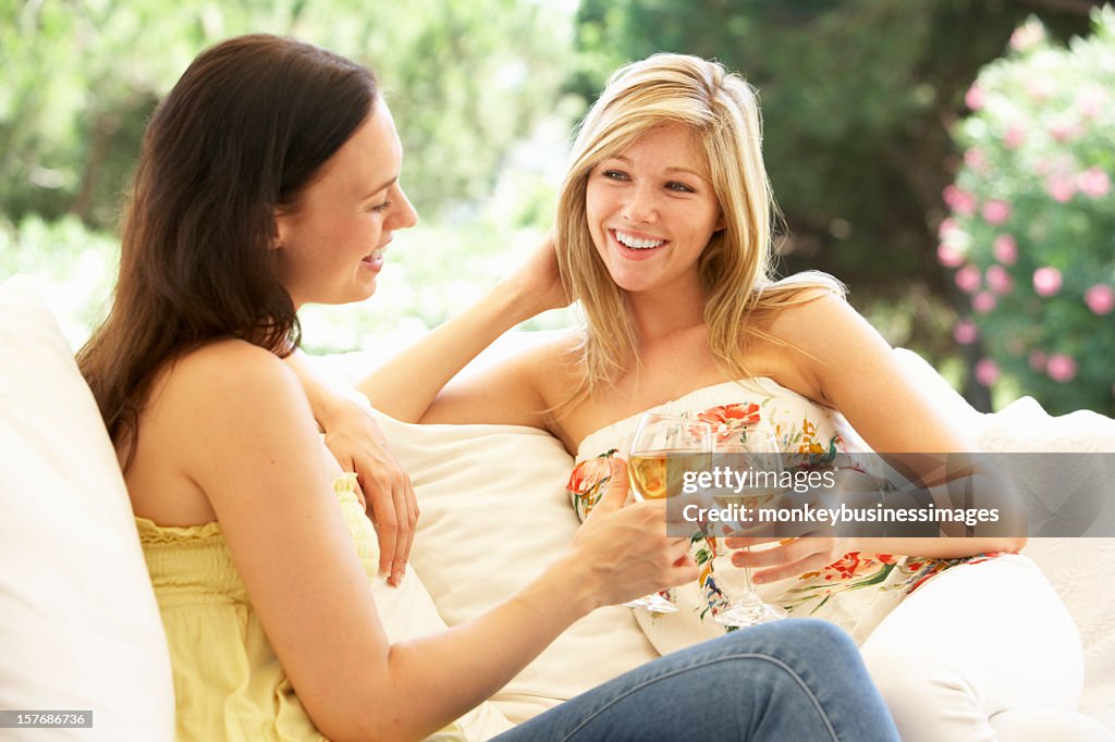 Two Female Friends Relaxing On Sofa With Glass Of Wine