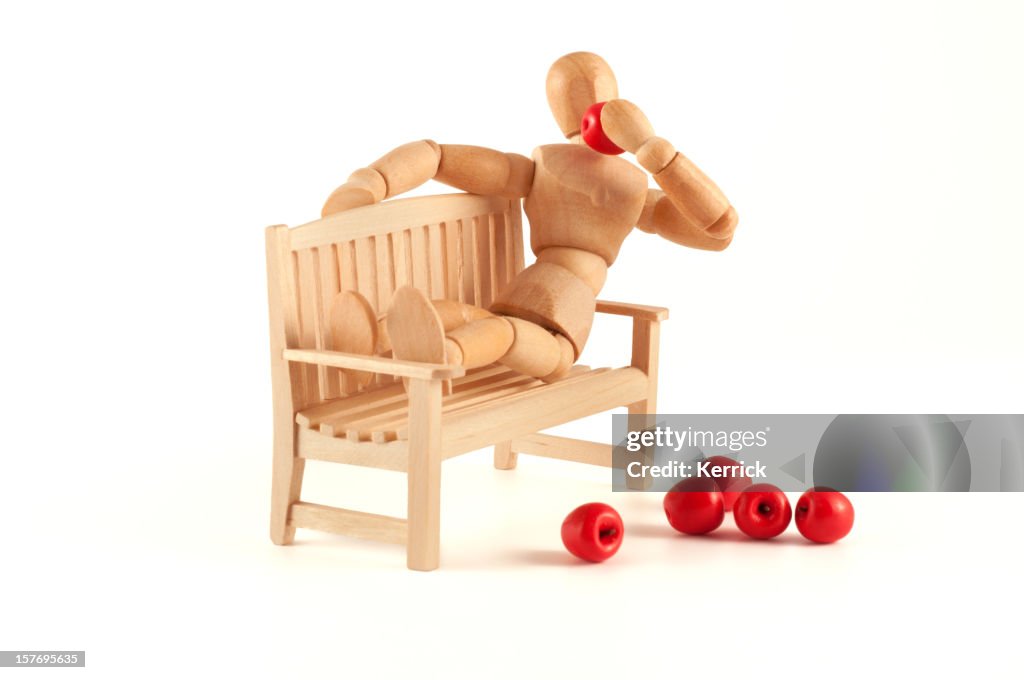 Wooden mannequin relaxing at a bench and eats apples