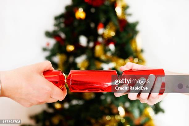 two hands pull a bright red christmas cracker - christmas cracker stock pictures, royalty-free photos & images