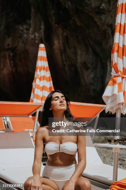 serene woman sits on a sun lounger on a beach - tomar el sol fotografías e imágenes de stock