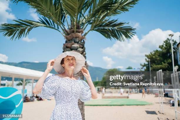 senior woman in a hat on a background of palm trees blue sky summer travel - blue white summer hat background stock pictures, royalty-free photos & images