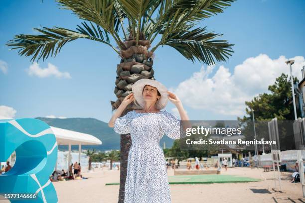 senior woman in a hat on a background of palm trees blue sky summer travel - blue white summer hat background stock pictures, royalty-free photos & images