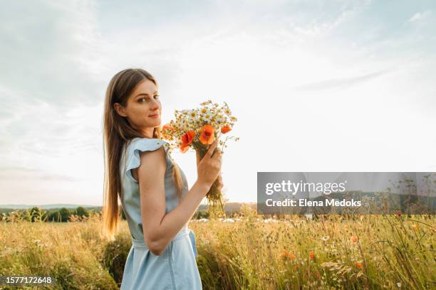 placated attractive young woman with a bouquet of field wild flowers stands contented in the field and enjoys nature - margarida imagens e fotografias de stock