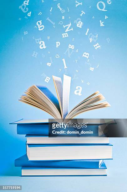 open book with flying, scattered letters isolated on blue background - abc news stockfoto's en -beelden