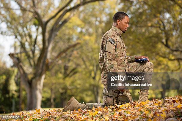 kneeling soldier praying over an american flag - soldier praying stockfoto's en -beelden