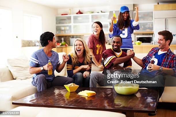 friends watching football in living room - american football team stockfoto's en -beelden