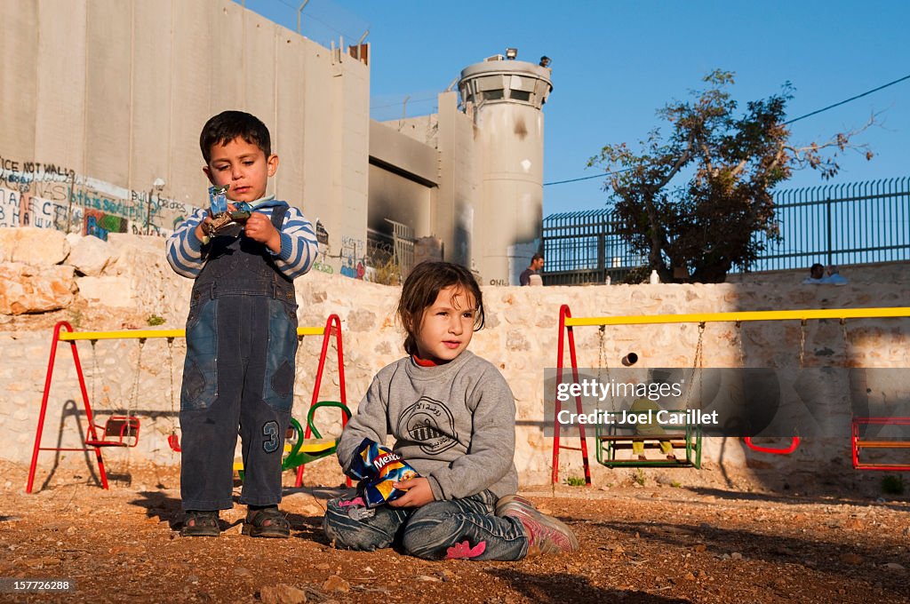 Palestinian children at playground beside Separation Barrier wall in Bethlehem