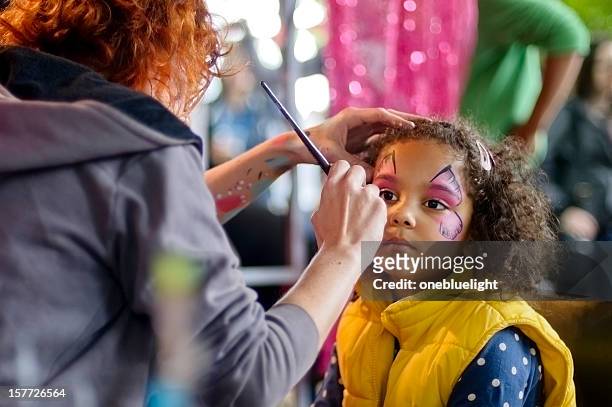 little girl of 5 is getting her face paint, outdoors - geschminkt gezicht stockfoto's en -beelden