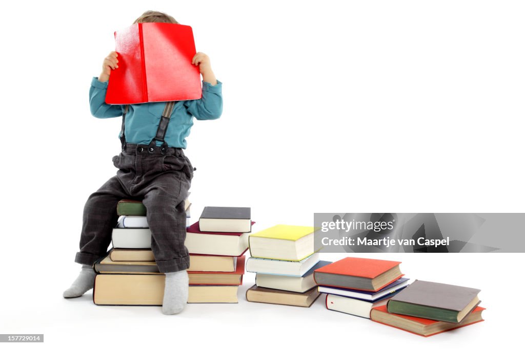 Cute baby Boy hiding behind a Big Red Book.